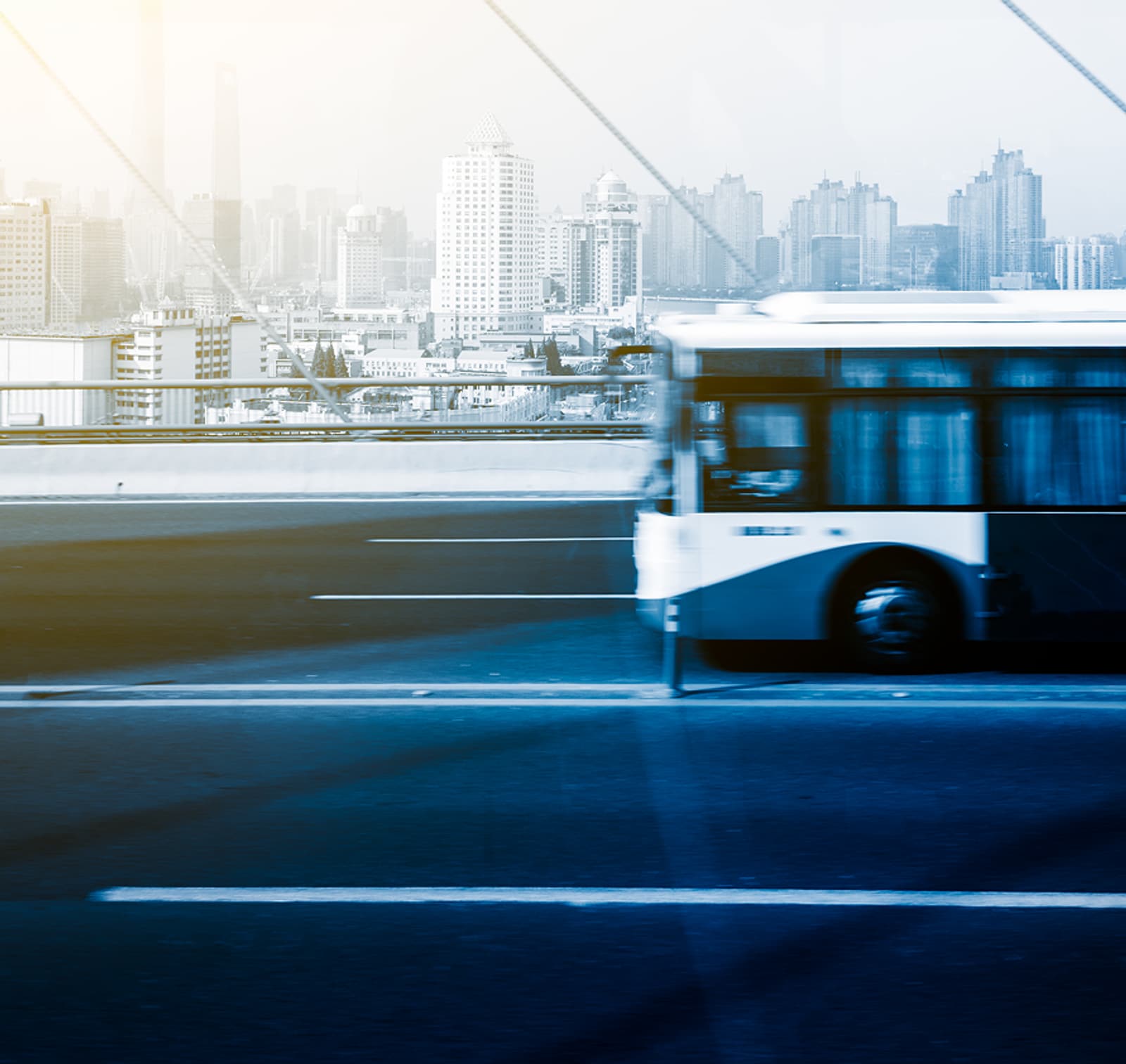 A city bus crossing a bridge at speed, city skyline behind it